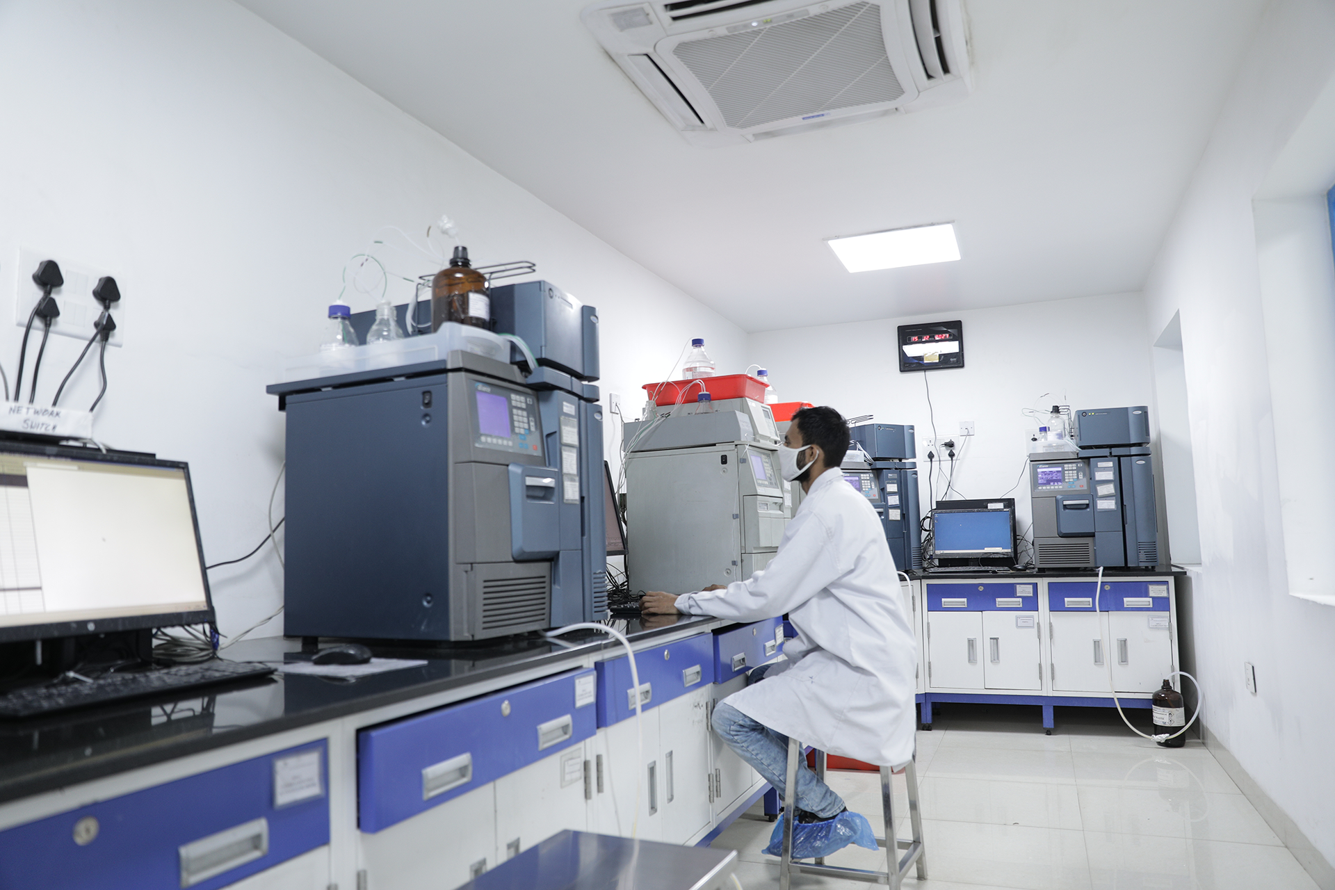 A stack of refurbished LC-MS and GC-MS equipment with glass bottles on top, connected by tubes to a black device with a blue stripe.